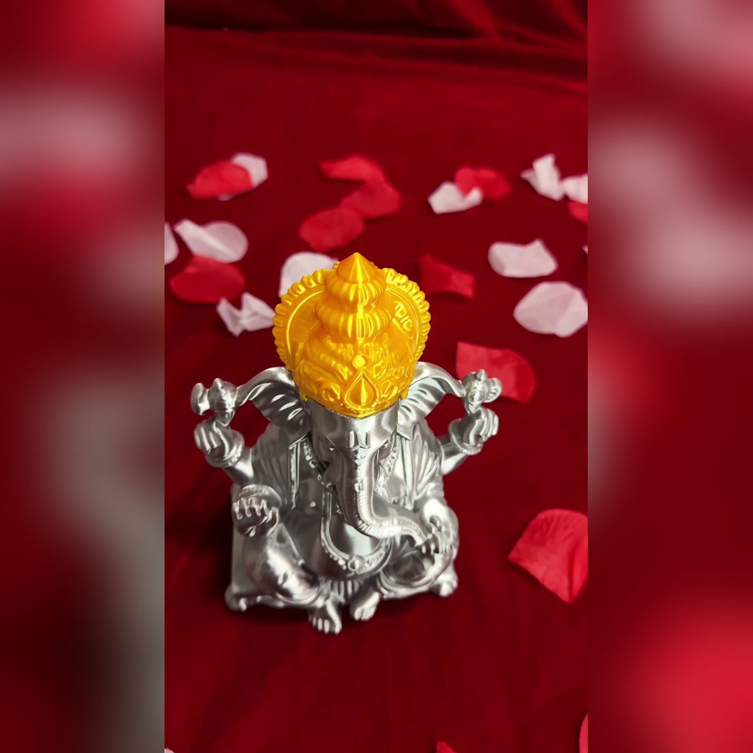Three-quarter view of the silver and gold 3D-printed Ganesh Ji idol on red cloth with petals