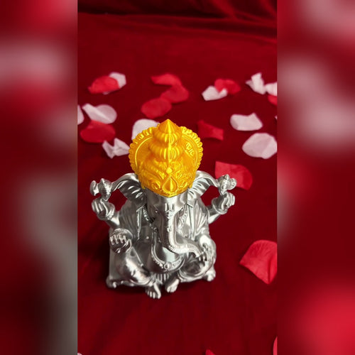 Three-quarter view of the silver and gold 3D-printed Ganesh Ji idol on red cloth with petals