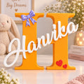 Personalized 3D printed big letter name sign — orange letter H with white script name Hanvika, purple bow and red hearts