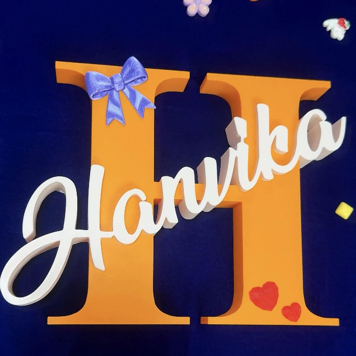 3D printed name sign — orange letter H with white script name Hanvika, purple bow and red hearts