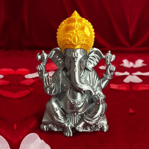 3D-printed Ganesh Ji idol in metallic silver with an ornate gold crown, displayed on red fabric with flower petals