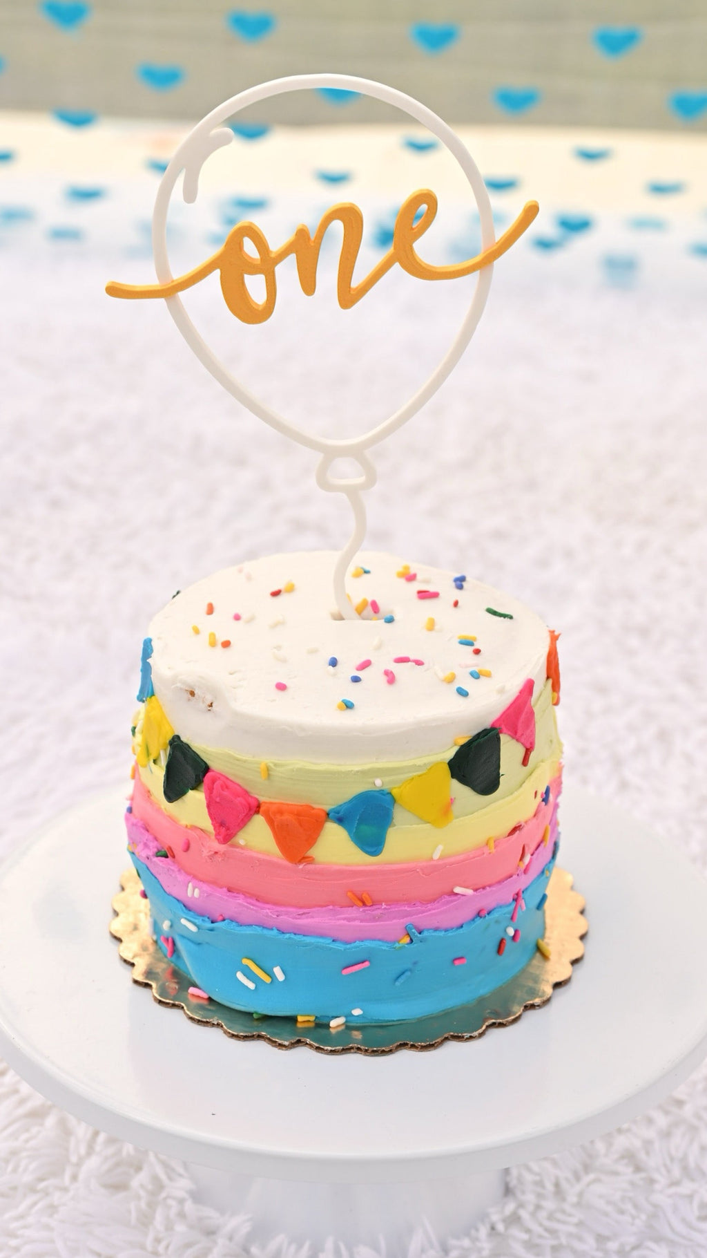Personalized balloon 'one' cake topper on rainbow smash cake, birthday decor