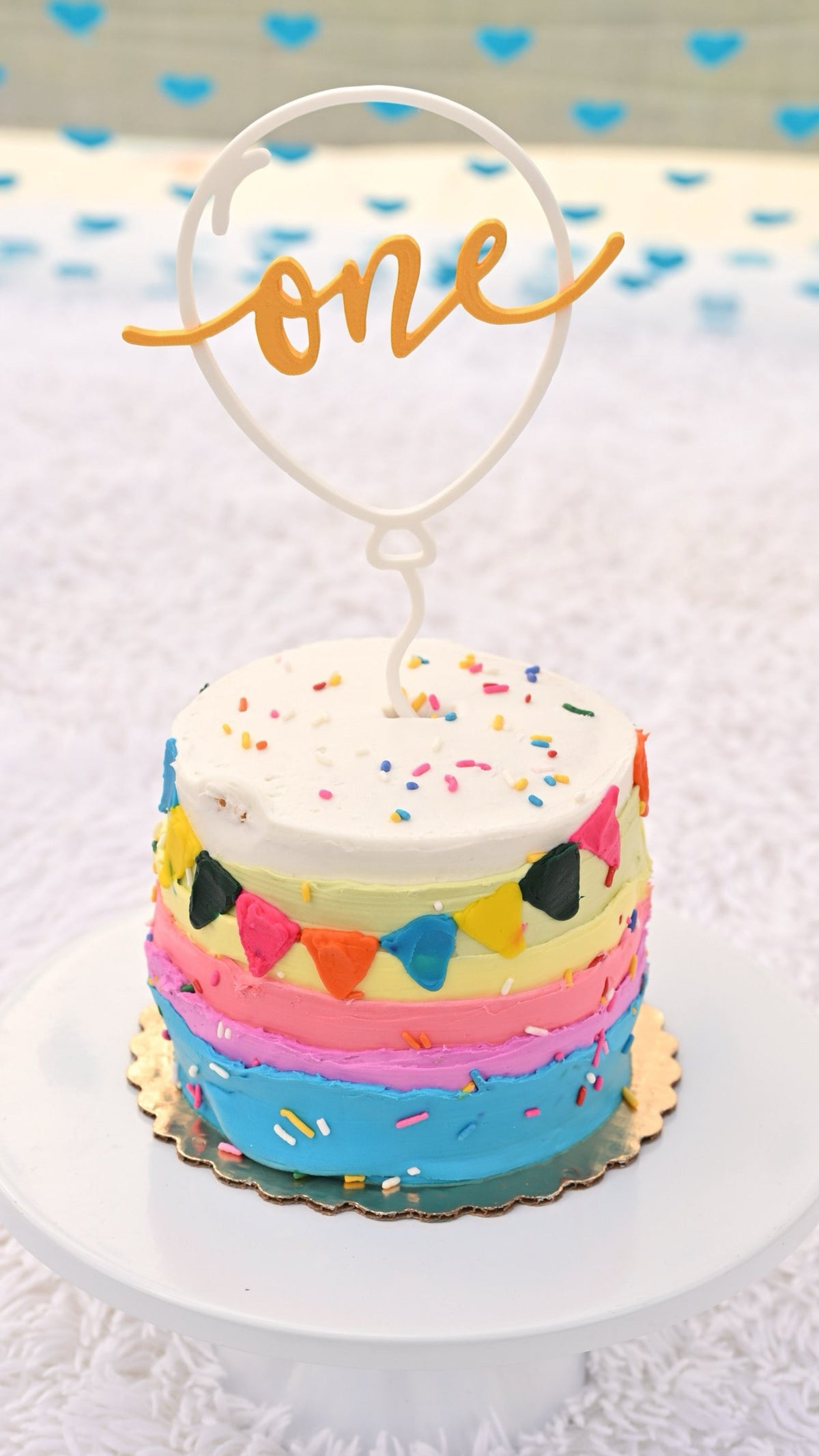 Personalized balloon 'one' cake topper on rainbow smash cake, birthday decor
