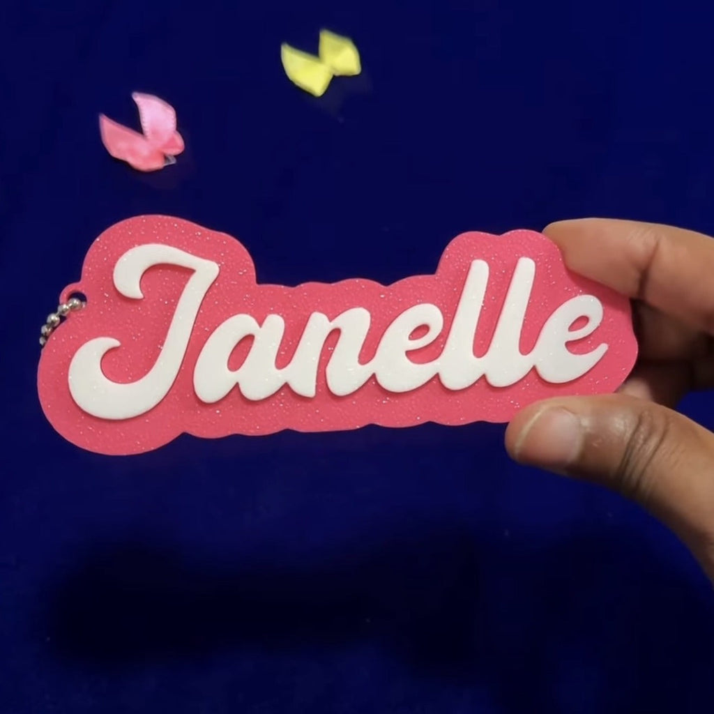 Personalized 3D printed name bag tag — pink tag with white name Janelle, held in hand