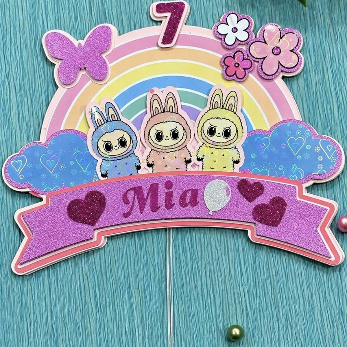 Personalized rainbow cake topper — pastel rainbow with bunny characters, number 7 and name Mia on a purple banner